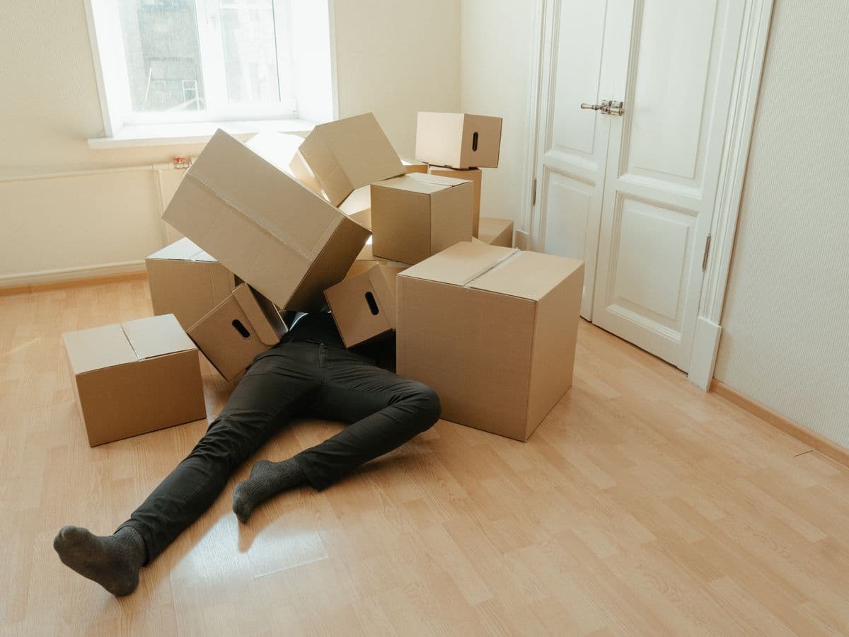 Stack of cardboard moving boxes toppled onto a person lying on the floor